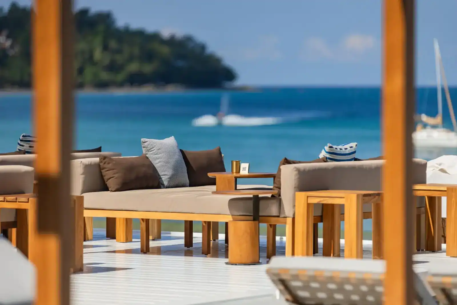 Teak daybeds on a white deck facing the turquoise sea of Bang Tao