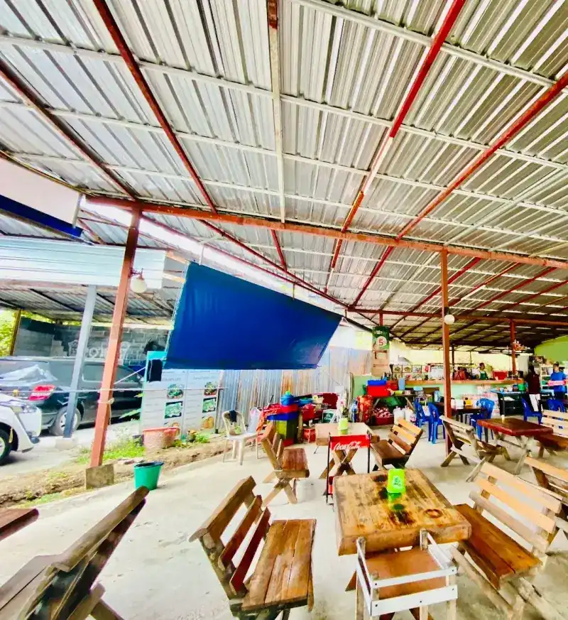 The open dining hall: wooden tables and benches under a high metal roof on a red steel frame