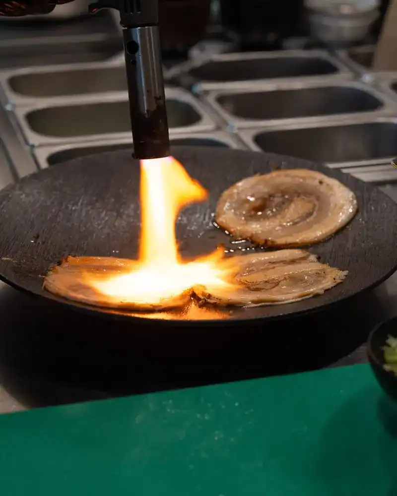 Slices of rolled chashu seared with a flame in the kitchen