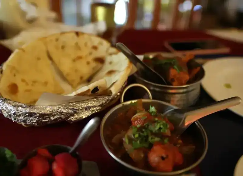 Naan in a foil-lined basket beside curries in steel bowls