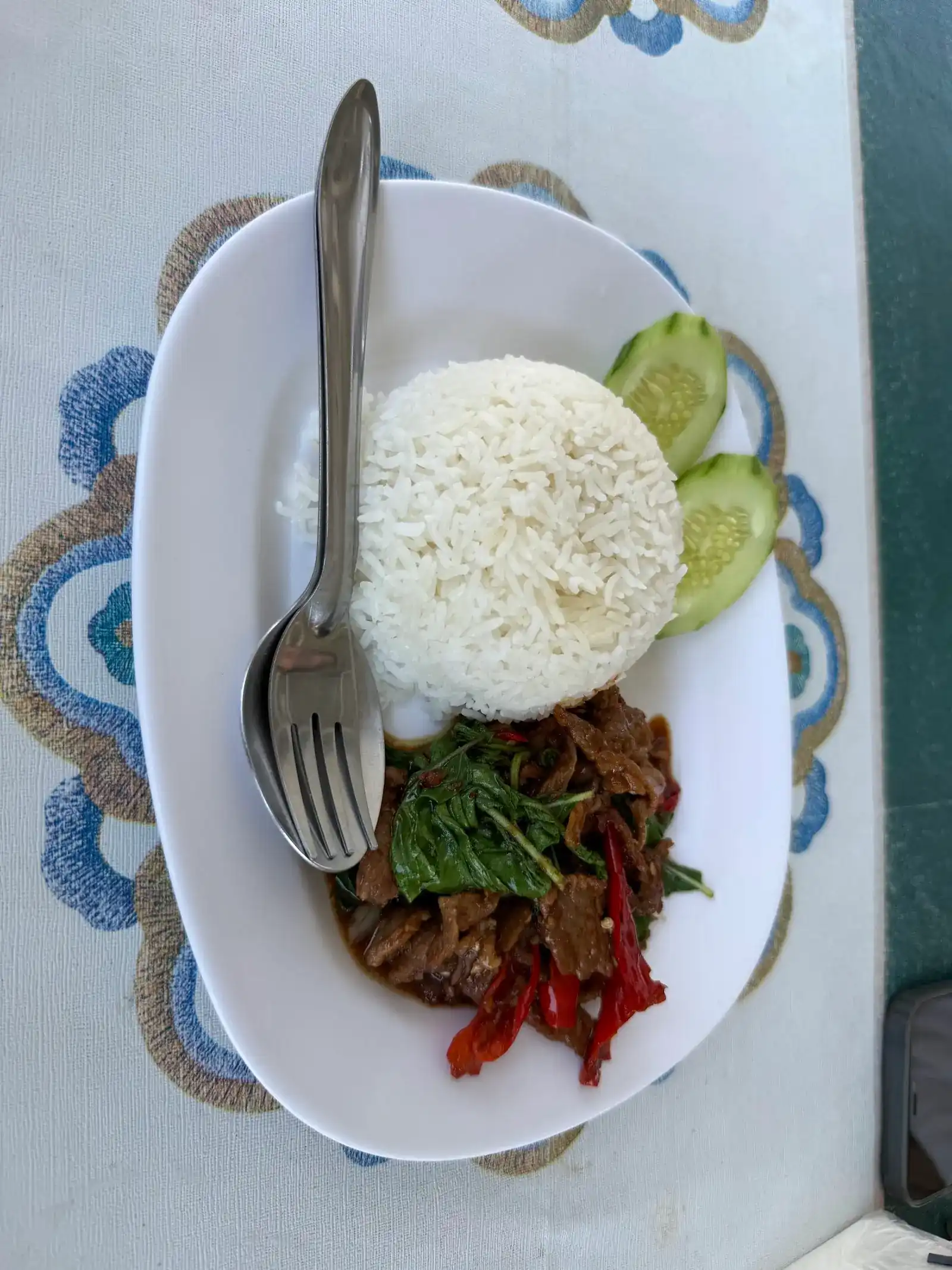 Holy-basil stir-fry with sliced meat and red chilli, a dome of rice and cucumber, on the blue-flowered tablecloth