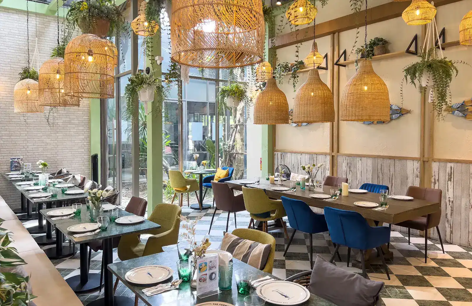 The dining room: rattan lamps and hanging plants over green stone tables, blue and olive chairs and a chequered floor