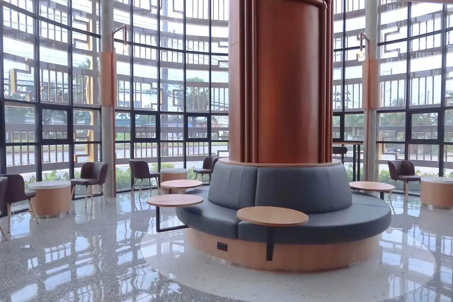 A ring of blue banquette around the copper column, in front of the tall steel-framed glass wall