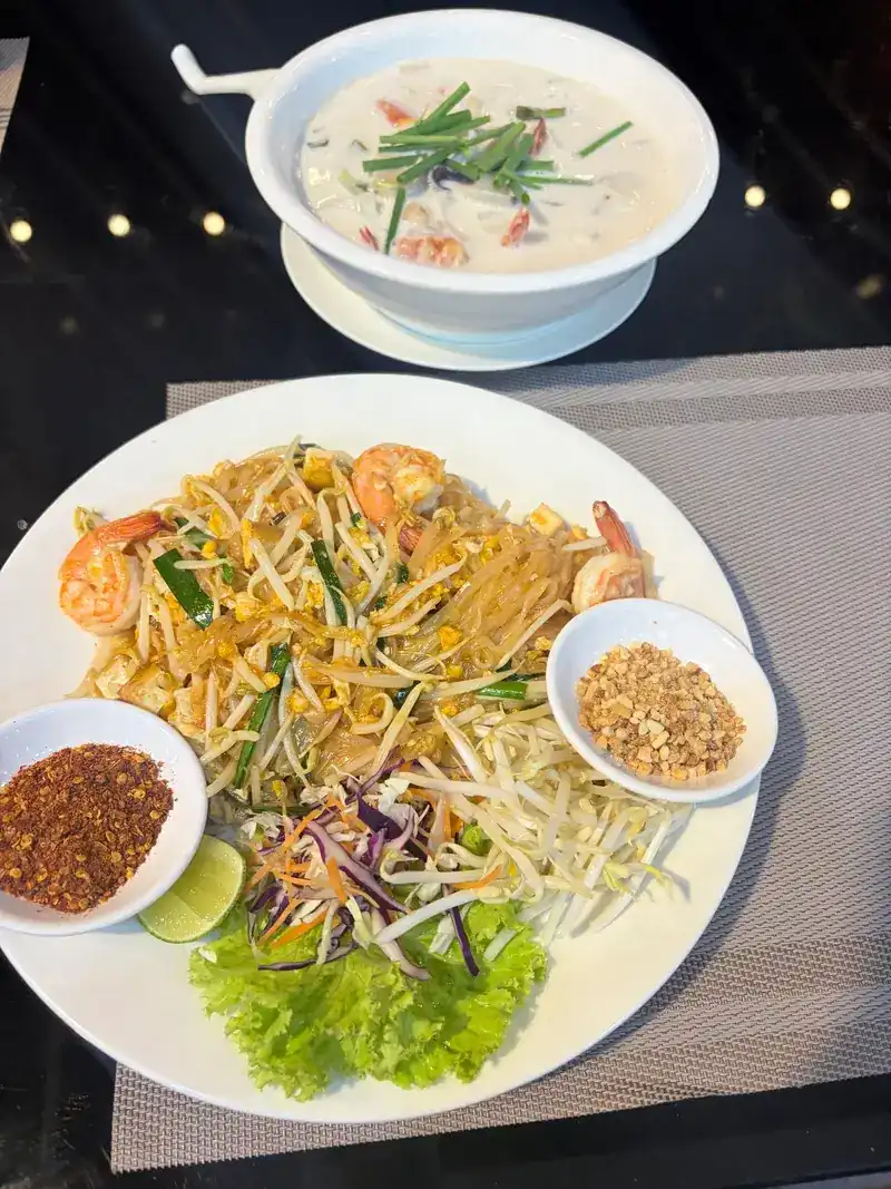 Pad thai with prawns, crushed peanuts and chilli flakes, with a bowl of coconut soup behind / ผัดไทยกุ้ง ถั่วลิสงป่น พริกป่น และซุปกะทิหนึ่งถ้วย