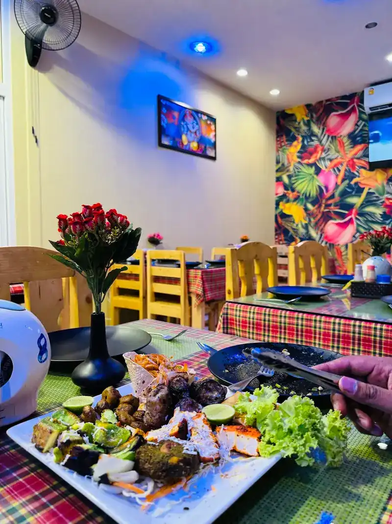 A grilled platter on a check tablecloth, red roses on the table and tropical flower wallpaper behind