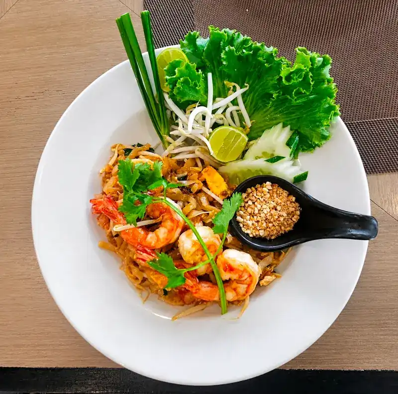 Pad thai with prawns, lime, bean sprouts and crushed peanuts on a white plate