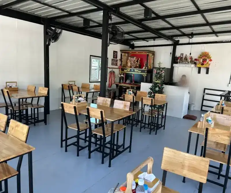 The rooftop room: wooden tables and chairs under a high steel roof, wall fans and a small shrine at the back