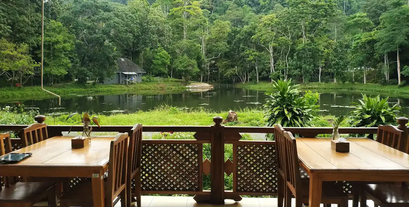 Two wooden tables at the carved lattice rail of the terrace, looking over the pond to the forested hills