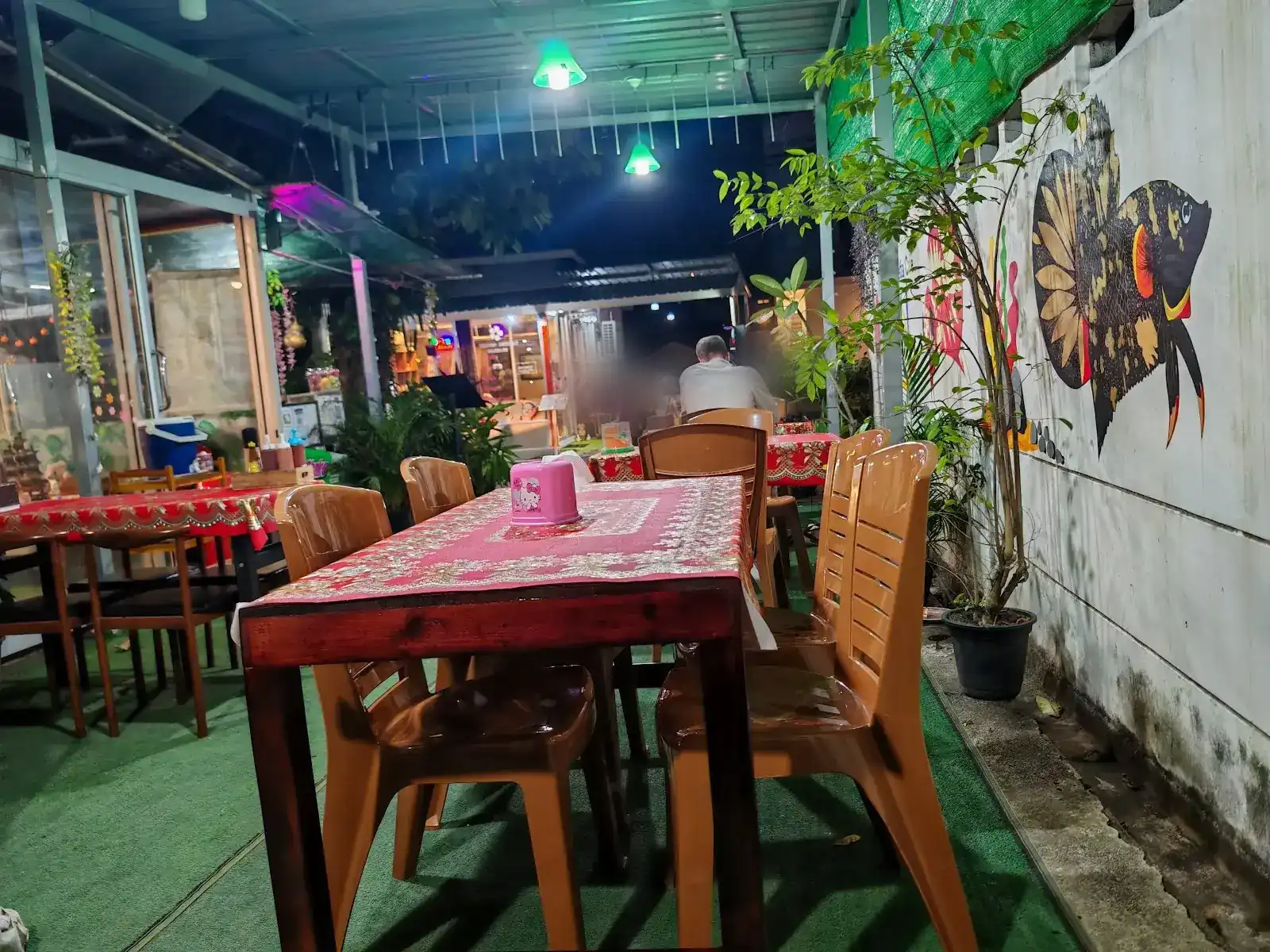 Tables with red cloths under green lamps, and a betta fish painted on the wall at Betta Cafe