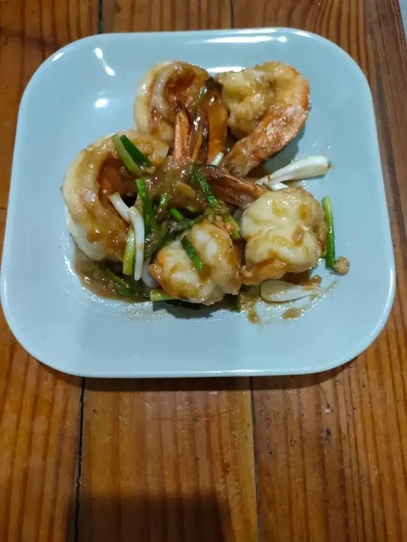 Prawns in a glossy sauce with spring onion on a blue plate