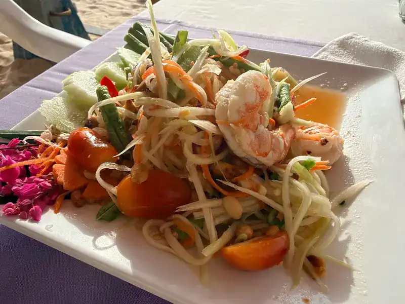 Green papaya salad with prawns, at a table by the sand