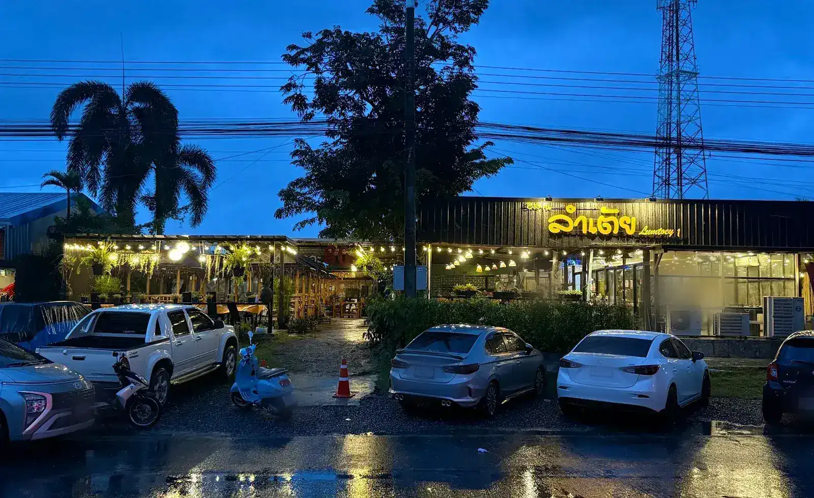 The restaurant at dusk on Don Jom Tao Road, its gold sign lit and rain on the road
