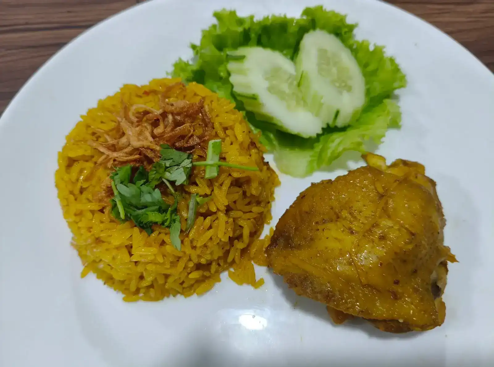 Khao mok gai: a mound of golden yellow rice topped with fried shallots and coriander, a piece of chicken, cucumber and lettuce