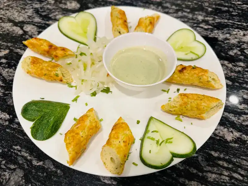 Grilled kebab pieces around a bowl of green dip, with cucumber cut into hearts