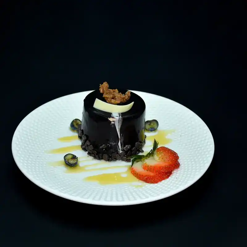A glazed chocolate dessert on a white plate with sliced strawberry