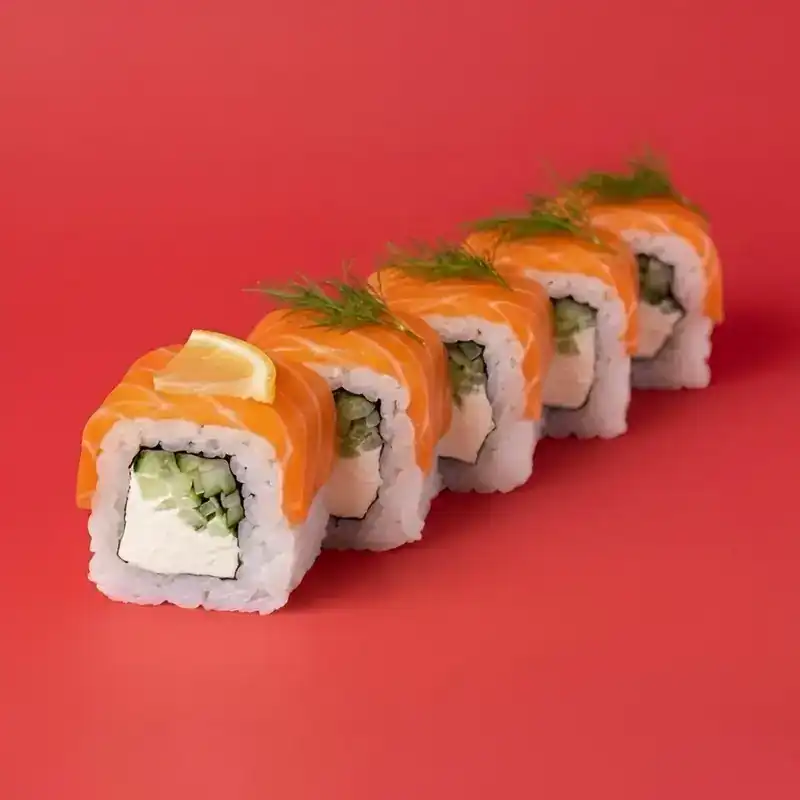 Salmon roll with cream cheese and cucumber, topped with dill, on a red background