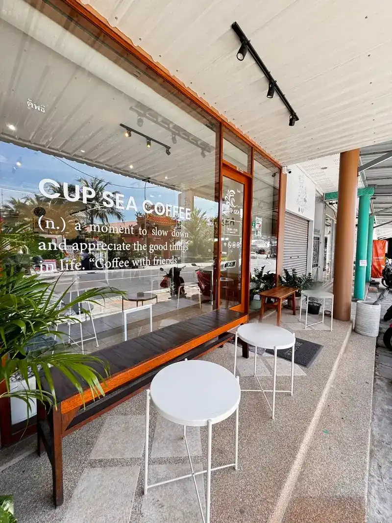 The café’s front on Kata Road: a big glass window with their words on it, a wooden bench and small white tables