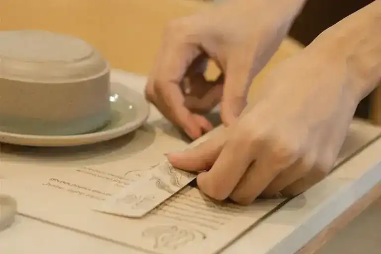 Hands setting a paper menu sheet on a table beside a bowl