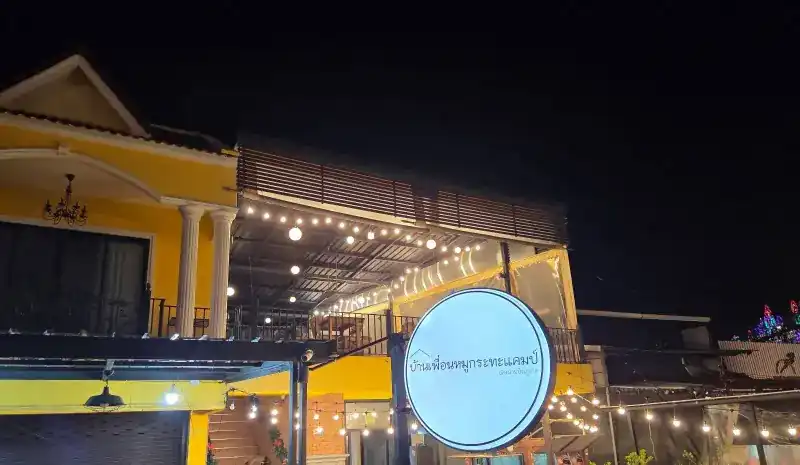 The yellow house at night, its upstairs terrace strung with bulbs and the round lit sign in front
