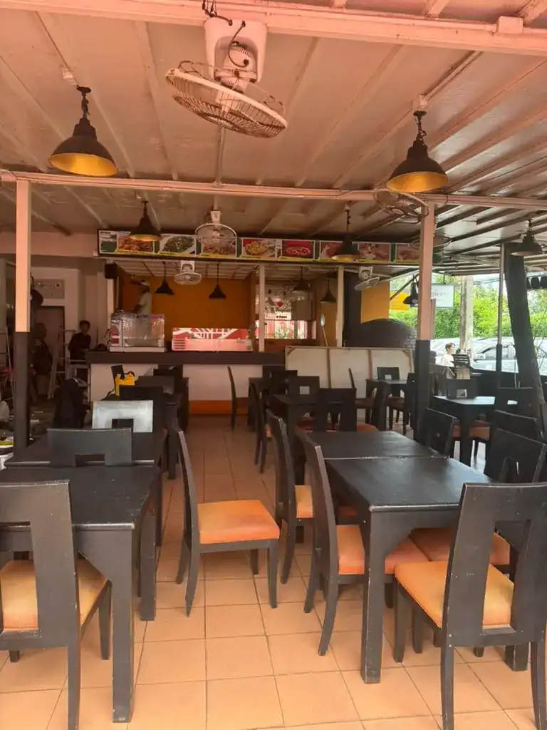 The dining room with dark wood tables, orange seats and the kitchen counter at the back