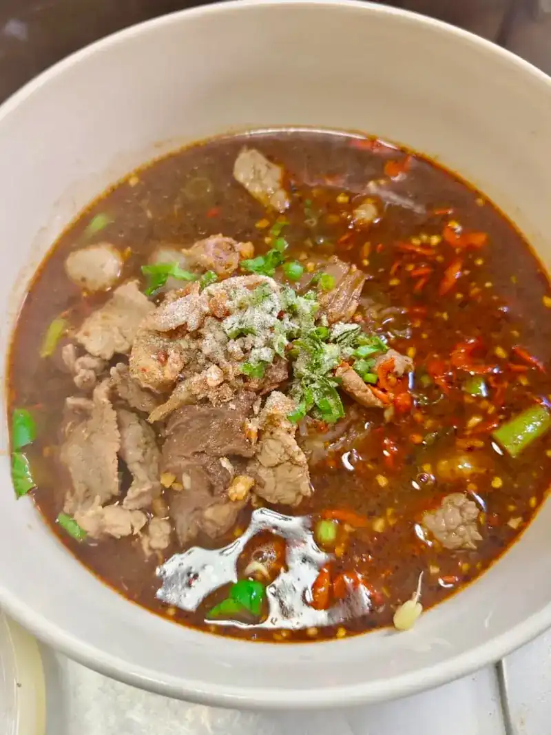 A bowl of boat noodles with sliced meat, chilli and spring onion