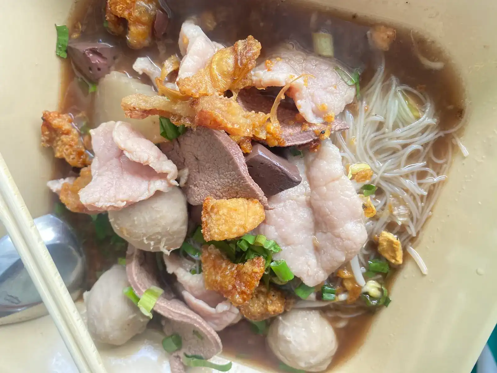 A bowl of noodle soup with rice vermicelli, sliced pork, liver, meatballs, crispy pork and spring onions