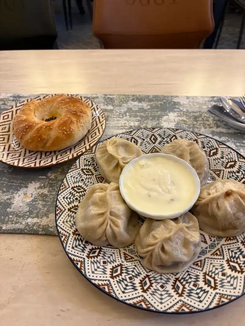 Manti dumplings around a bowl of white sauce, with a ring of sesame bread