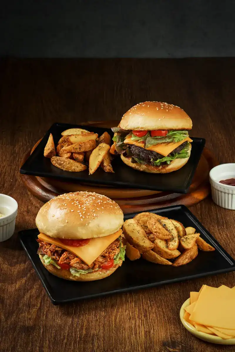 Two burgers with potato wedges on black plates