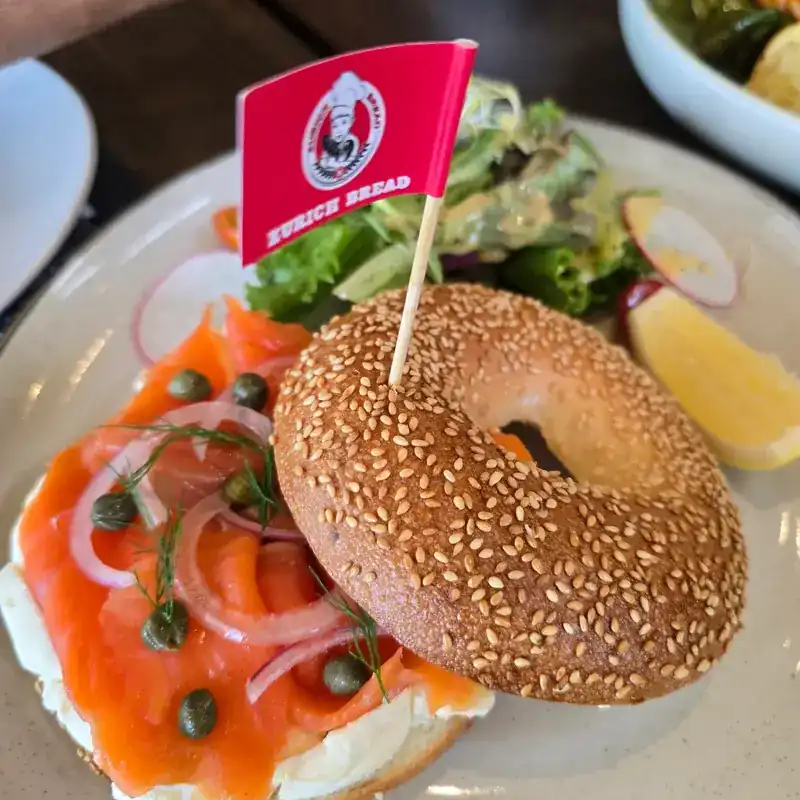 A sesame bagel with salmon, capers, red onion and cream cheese, with salad
