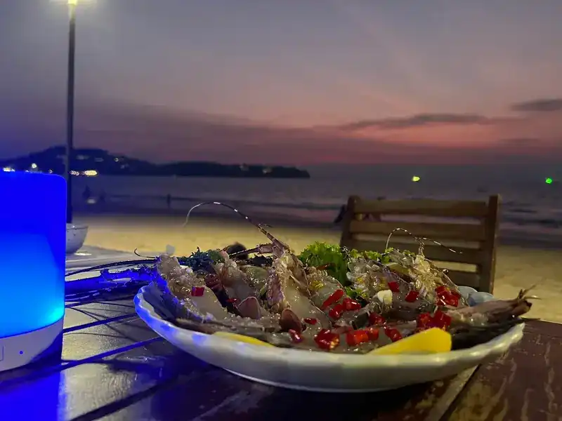A plate of raw prawns with chilli and lemon on a table by the sea at sunset