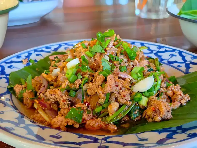 Larb with herbs and spring onion on a banana leaf, on a blue-and-white plate