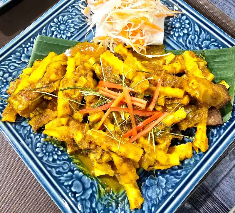 A yellow curry stir-fry on banana leaf and a blue patterned plate