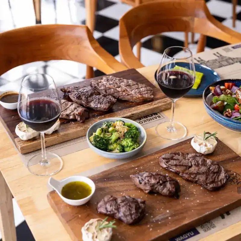 Grilled steaks on two wooden boards with broccoli, a salad and olive oil on a table in the restaurant