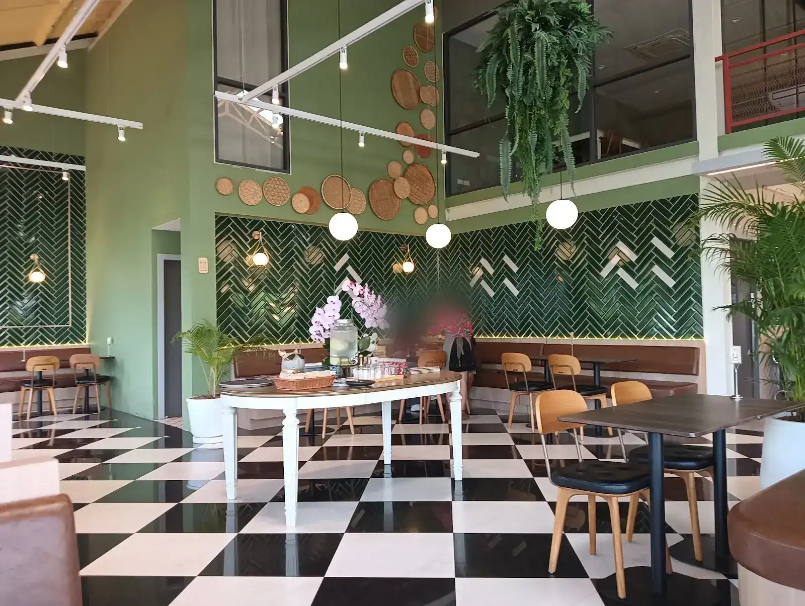 The dining room: green herringbone tiles, a black and white checkered floor, wooden chairs and hanging ferns