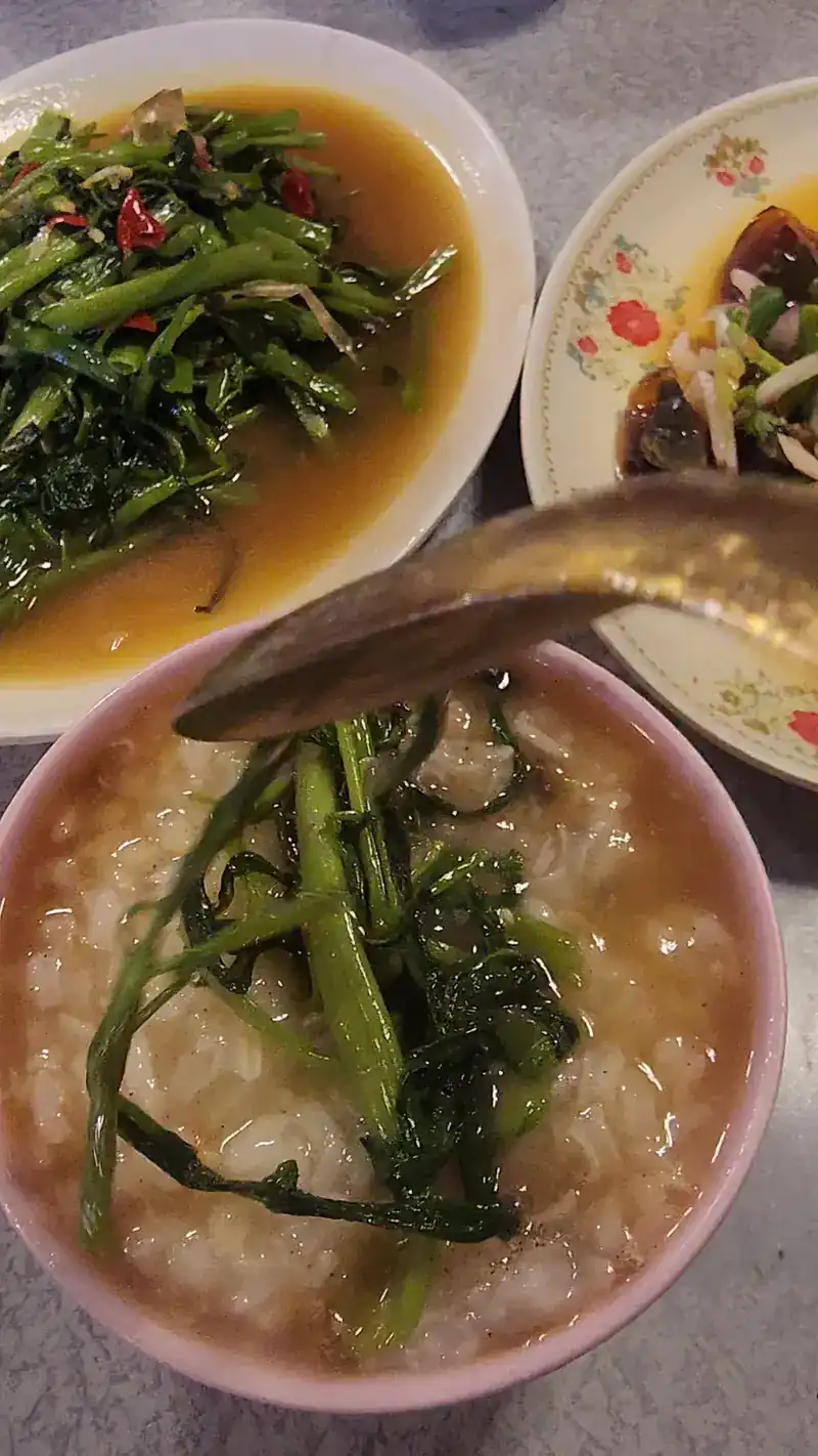 Rice soup in a pink bowl with stir-fried water spinach spooned on top