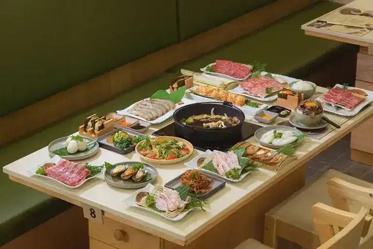 A table laid for suki: a pot in the middle, surrounded by plates of sliced meat, fish, seafood and small dishes