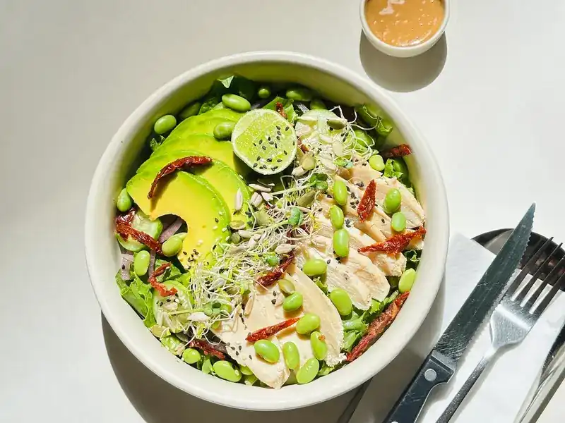 A bowl of greens with avocado, edamame, sprouts and lime
