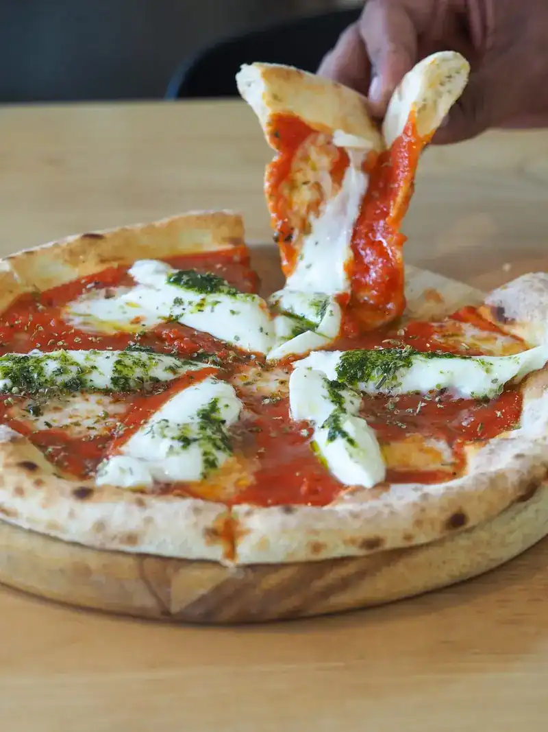A hand pulling a slice from a pizza with tomato sauce and melted white cheese