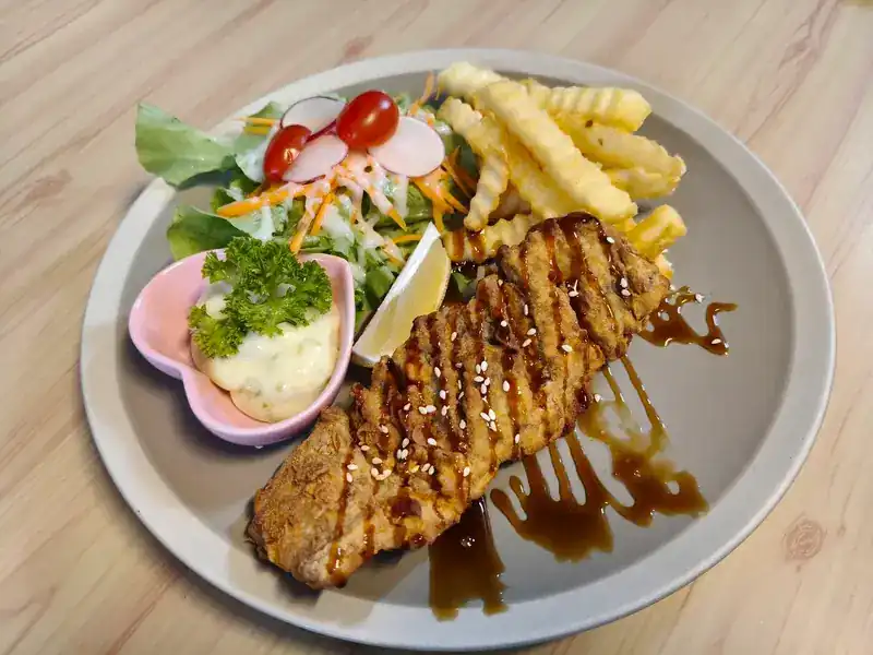 Steak with a sweet glaze and sesame, salad, lemon, crinkle-cut fries and a creamy sauce in a pink heart-shaped dish
