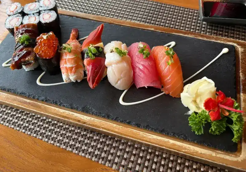Nigiri and maki on a slate board with a line of sauce and a red flower / นิกิริและมากิบนแผ่นหินชนวน มีเส้นซอสและดอกไม้สีแดง