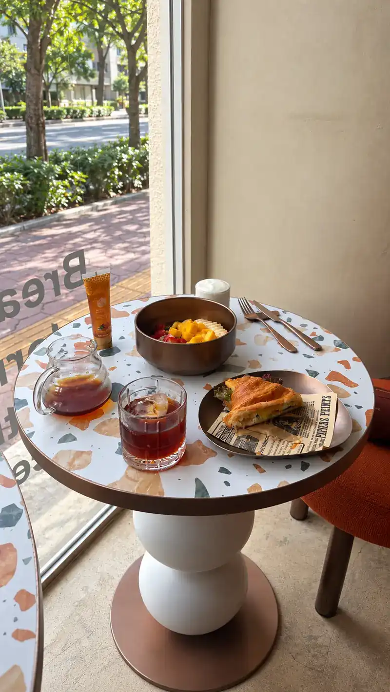 A small terrazzo table by the window with a bowl, a pastry and cold drinks
