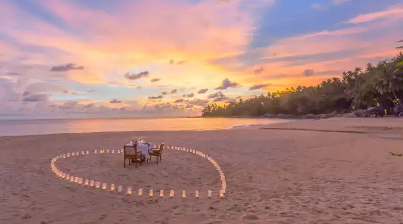 A table for two inside a heart of candles on the sand at sunset