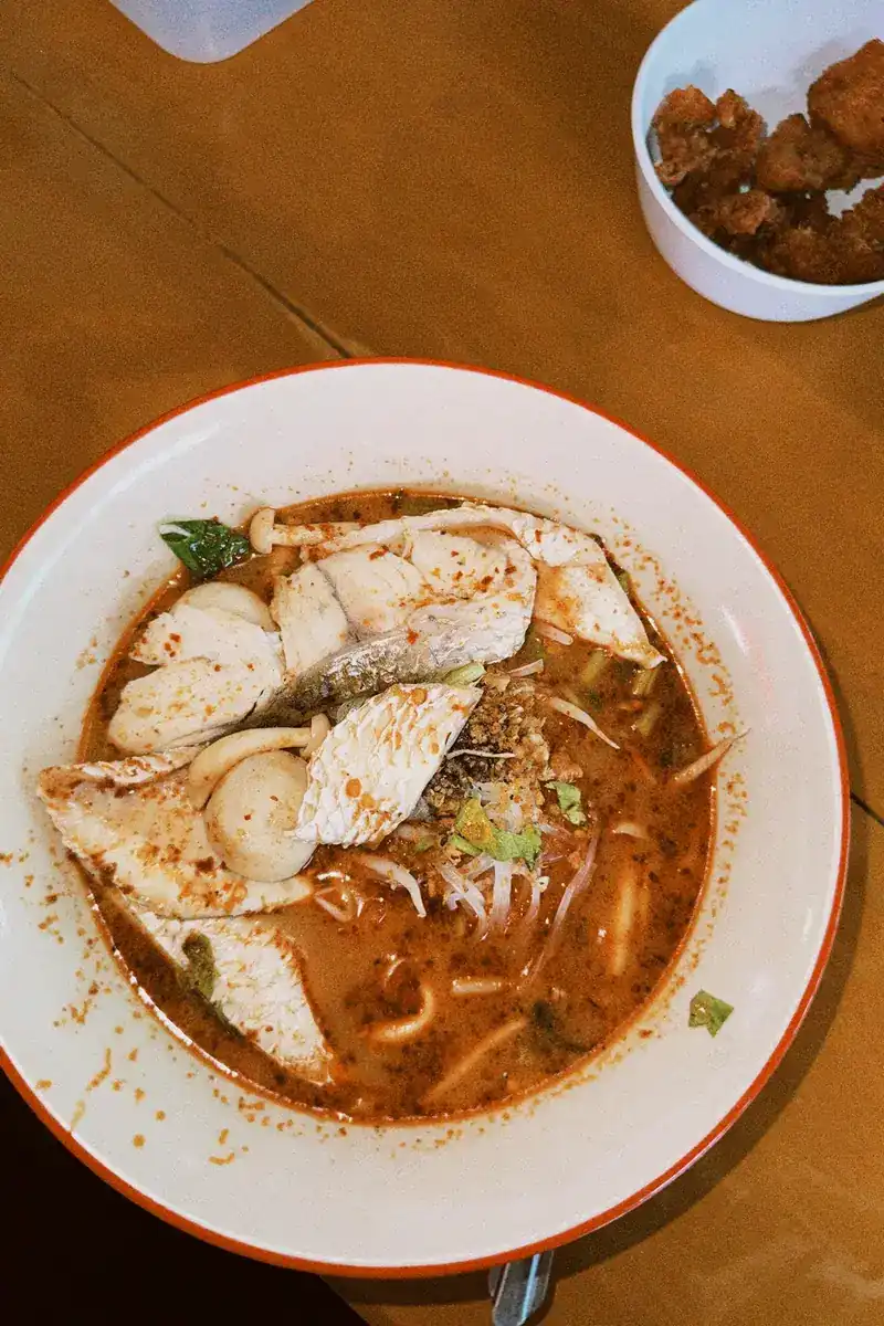 A bowl of noodle soup in a red broth with slices of fish and fish balls