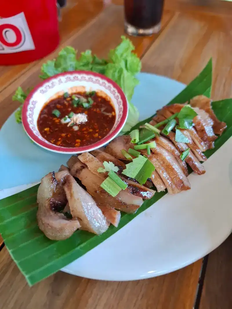Sliced grilled pork on banana leaf with a bowl of chilli dipping sauce