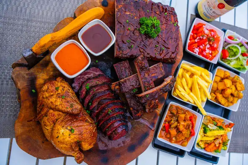 A sharing board with grilled chicken, sliced steak and ribs, with fries, potatoes and salads