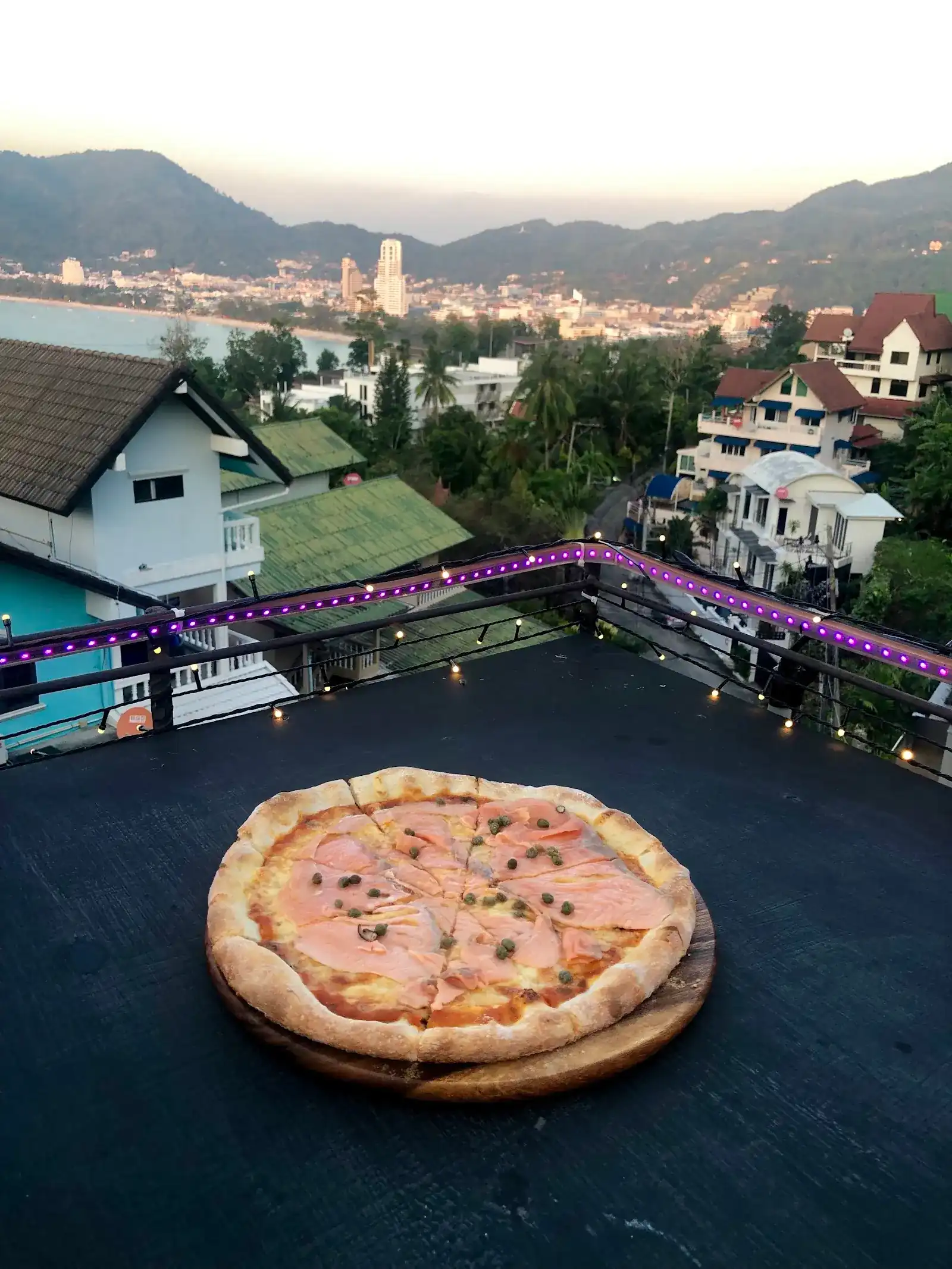 Smoked salmon and caper pizza on the terrace ledge, with Patong town and beach below