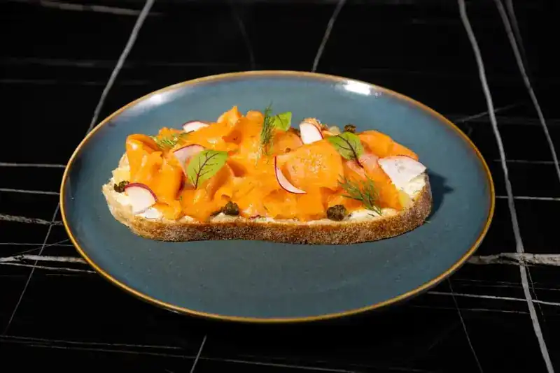 Salmon toast with radish, capers and dill on a blue plate