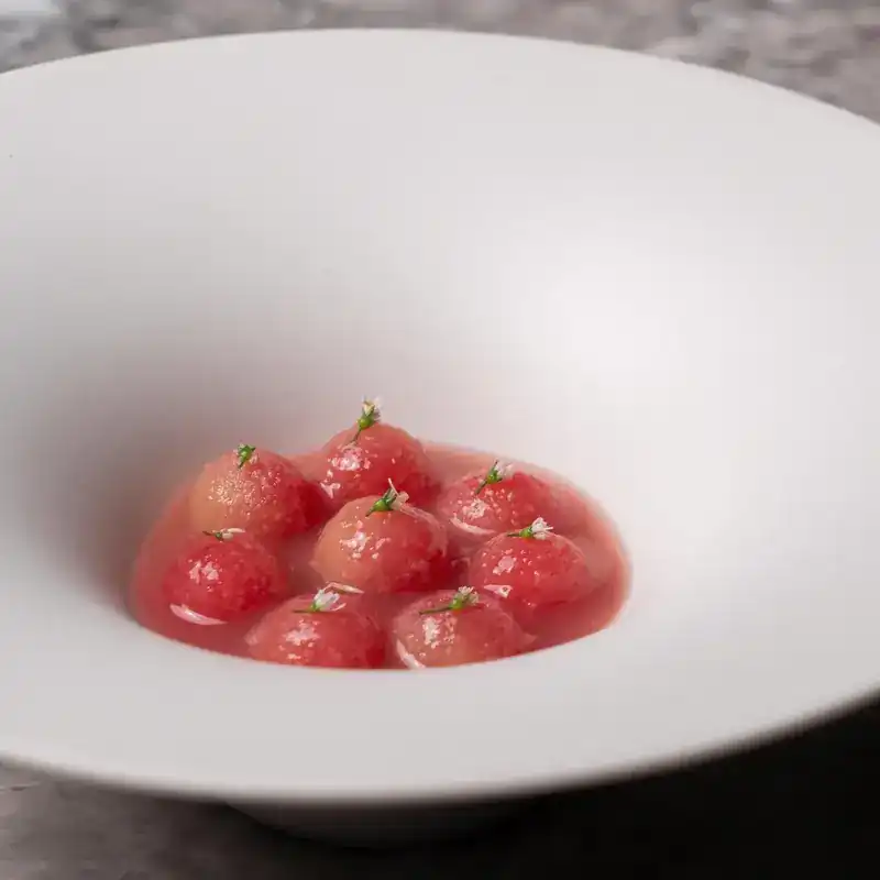 Pink spheres in a pale pink broth, in a wide white bowl