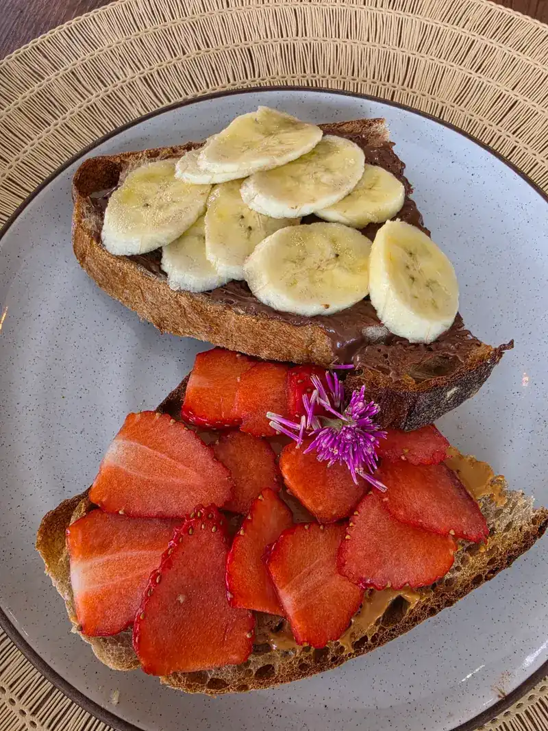 Two slices of toast, one topped with banana, one with strawberries