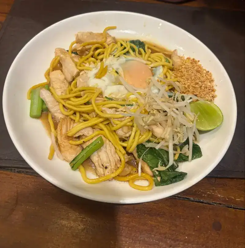 Stir-fried egg noodles with chicken, a fried egg, peanuts and lime
